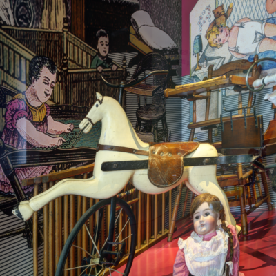 Ein Holzpferd und eine Mädchenpuppe in der Kinderwagenausstellung