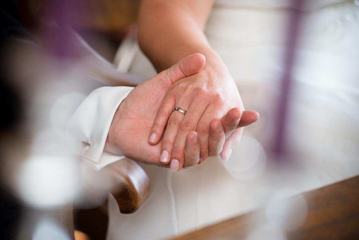 Zwei Hände von einem frisch vermählten Paar sind nah zu sehen. An der Hand der Frau ist en Ring zu sehen.